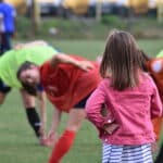 petite fille de dos devant un entrainement de joueuses de football plus âgées